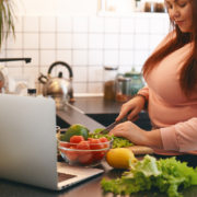 Een vrouw met een roze t-shirt staat in de keuken en snijdt groenten die op het aanrecht liggen, tegen overgewicht.