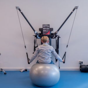 kinderfysiotherapie Jongen met zijn rug naar de camera toe zit op een bal en doet aan oefeningen voor kinderfysiotherapie